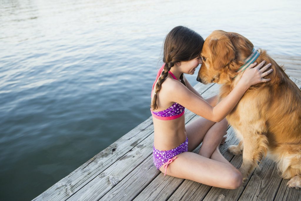 A young girl and a golden retriever dog sitting on a jetty.